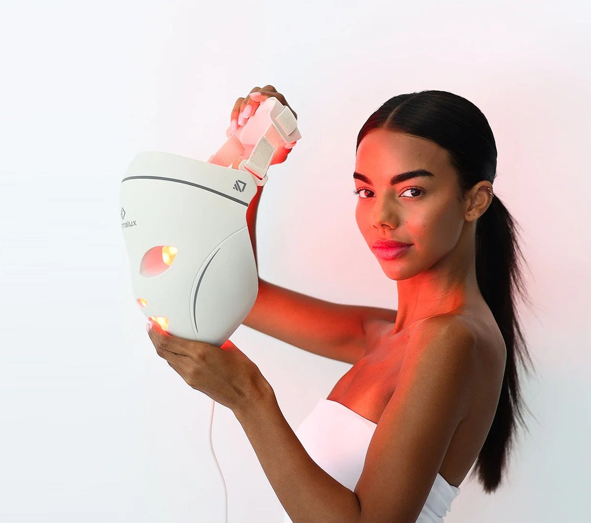 A woman holding the Dermalux LED face mask beside her face, red light activated